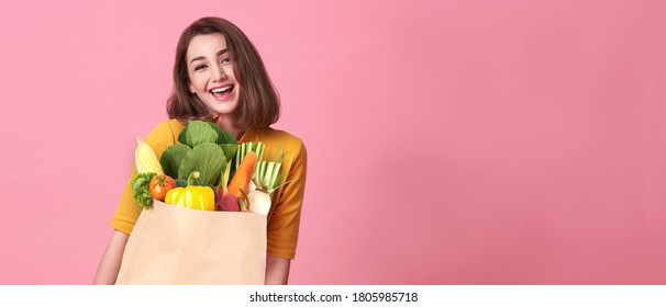 Happy Woman Holding Paper Bag Full Of Fresh Vegetable Groceries Isolated On Pink Copy Space Background.