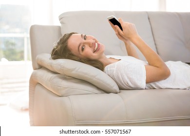 Happy Woman Holding Phone While Laying Down On Sofa