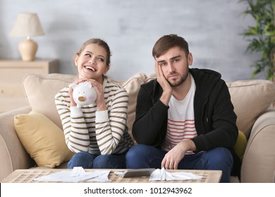 Happy Woman Holding Piggy Bank And Sad Man With Bills At Home. Money Problems In Relationship