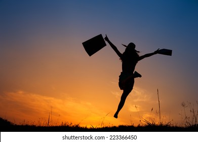 Happy Woman Holding Shopping Bags Jumping In Sunset Silhouette