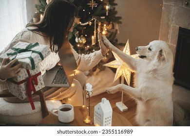 Happy woman holding stylish christmas gifts with credit card and playing with cute white dog in festive decorated christmas room with lights. Christmas shopping online and black friday sales. - Powered by Shutterstock