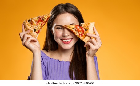 Happy woman holding two slices of pizza near face and smiling, concept of pizzeria advertisement, fast food delivery and eating out, orange background