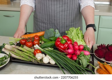 Happy Woman Holds A Tray With Fresh Vegetable Ingredients In The Kitchen Background. Closeup Healthy Vegan Food. 