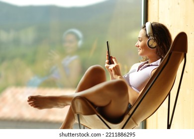 Happy woman at home or hotel listening to music sitting on a chair looking through a window - Powered by Shutterstock