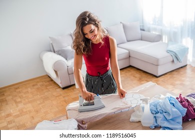 Happy Woman Housewife Ironing Clothes Iron In Laundry At Home. Happy Woman Ironing Cloth With Electric Iron In Kitchen. Housewife Bringing A Huge Pile Of Laundry On The Ironing Board