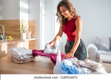 Happy Woman Housewife Ironing Clothes Iron In Laundry At Home. Happy Woman Ironing Cloth With Electric Iron In Kitchen. Housewife Bringing A Huge Pile Of Laundry On The Ironing Board