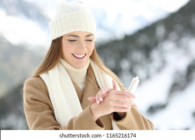 Happy Woman Hydrating Hands Skin With Moisturizer Cream In A Snowy Mountain In Winter