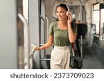 Happy woman immerses in online music utilizing headphones traveling in city tram, smiling and looking aside. Comfortable public transportation and daily commute leisure concept