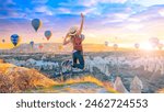 Happy woman jumping in air- beautiful sunrise Cappadocia landscape with hot air balloons flying in the sky