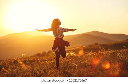 Happy woman jumping and enjoying life in field at sunset in mountains - Shutterstock ID 1352173667