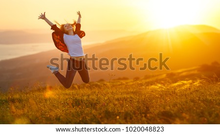 Happy woman jumping and enjoying life in field at sunset in mountains