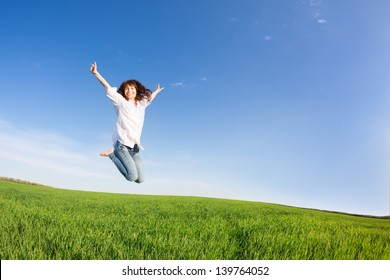 Happy Woman Jumping In Green Field Against Blue Sky. Summer Vacation Concept