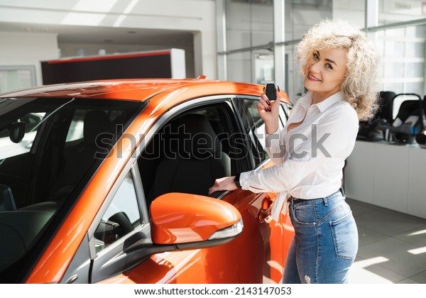 Happy woman\
with key near her new car in\
dealership