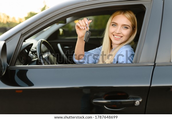 Happy woman with\
keys in car, driving\
school