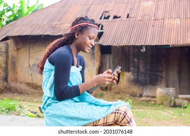 A happy woman or lady sitting and using a smart phone as she sits outside a village mud house
