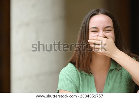 Happy woman laughing covering mouth looks at you in the street