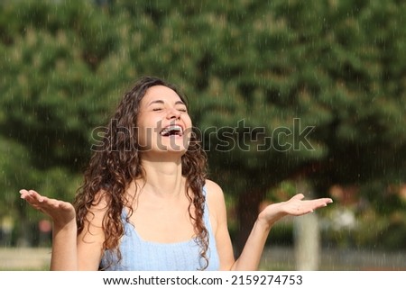 Happy woman laughing and enjoying under sudden rain in a sunny day