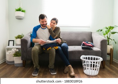 Happy woman leaning and embracing her boyfriend while he folds clothes after doing all the laundry at home - Powered by Shutterstock