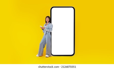 Happy Woman Leaning On Big Giant Smartphone With Empty White Display, Casual Female Holding Using Cell Phone, Browsing Website Advertising App, Yellow Background Mock Up, Full Body Length Banner - Powered by Shutterstock