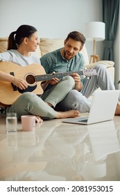 Happy Woman Learning To Play Acoustic Guitar With Help Of Her Husband At Home. Copy Space. 