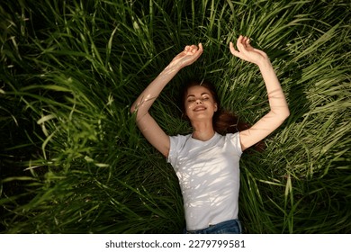 happy woman lies in high grass lit by the sun stretching her hands to the camera - Shutterstock ID 2279799581
