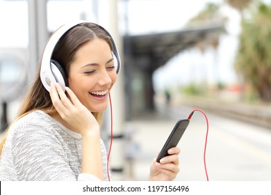 Happy woman listening online music with a smart phone and headphones in a train station - Powered by Shutterstock