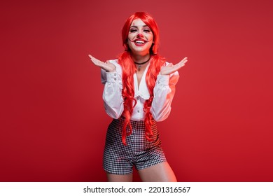 Happy Woman With Long Colored Hair And Clown Makeup Pointing With Hands Isolated On Red