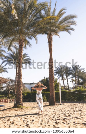 happy woman in long dress and hat walking on sand near ocean 