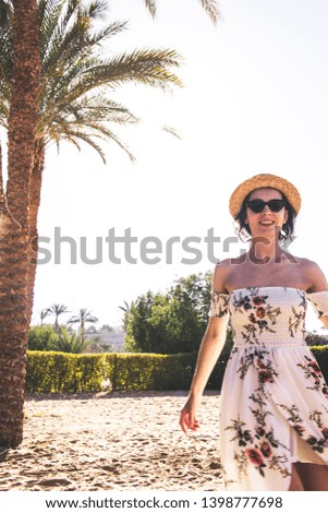 happy woman in long dress and hat walking on sand near ocean 
