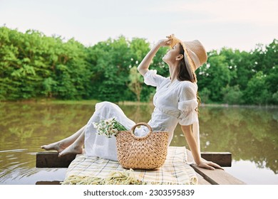 happy woman in a long light dress is resting by the lake sitting on a plaid and enjoying the view - Powered by Shutterstock