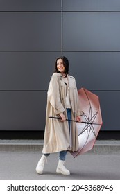 Happy Woman In Long Raincoat Looking Back While Posing With Red Umbrella