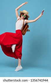 A Happy Woman In A Long Red Skirt Sneakers Raised Her Leg Up And Dancing On A Blue Background                  