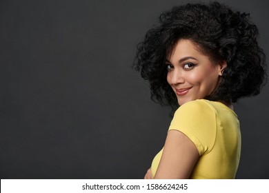 Happy woman looking at camera over shoulder smiling, over grey background