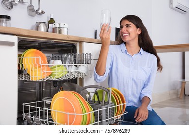 Happy Woman Looking At Clean Glass Crouching Near Dish Washer