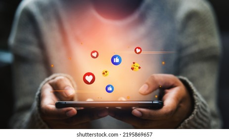 Happy woman looking on smartphone watching social and online entertainment, shopping, paying money in the digital world with fun and happiness emoticons, Social media and digital online concepts. - Shutterstock ID 2195869657