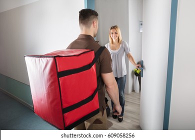 Happy Woman Looking At Pizza Delivery Man With Large Red Bag At Doorstep