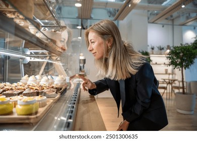 Happy woman looking at snacks for coffee, standing at showcase in cozy small cafe, going to buy purchase lunch, breakfast. Satisfied cheerful businesswoman at window display in coffeehouse, bakehouse. - Powered by Shutterstock