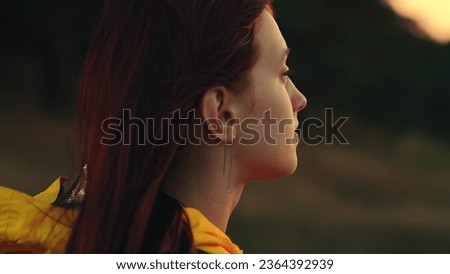 Happy woman looks around contemplating nature beauty at sunset light closeup. Woman traveler enjoys tranquility of wilderness in autumn park. Positive woman on day off tour to wild nature at twilight