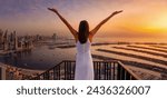 A happy woman looks at the panoramic view of the Dubai Marina district and the Palm island during golden sunset time, UAE