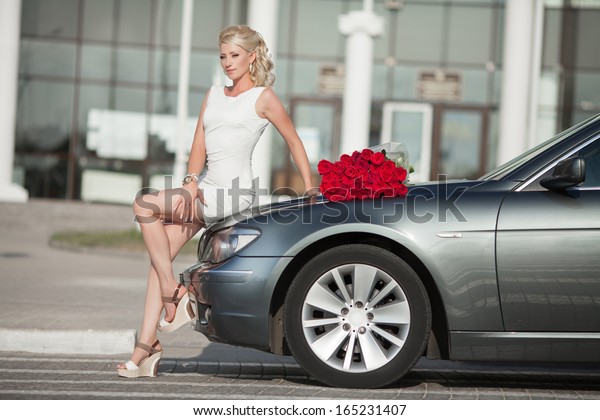 Happy woman\
in luxury car with roses flowers at Valentine\'s day. Sexy woman\
with bouquet in car. Beautiful rich woman smiling portrait. Sensual\
young girl with car. soft light\
shot.