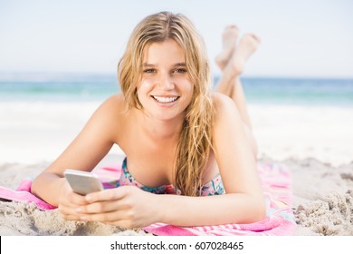 Happy woman lying on the beach and using mobile phone on a sunny day