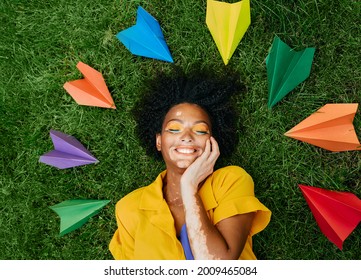 Happy woman lying on the green grass dreaming about vacation and travel, colored paper planes around her head. Travel concept - Shutterstock ID 2009465084