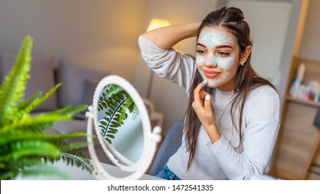 Happy Woman Making Facial Massage With Organic Face Scrub And Looking At Mirror At Home. Girl Applying Scrub Cream, Peeling And Cleaning Skin. Skin Care. Attractive Girl With Moisturizing Facial Mask