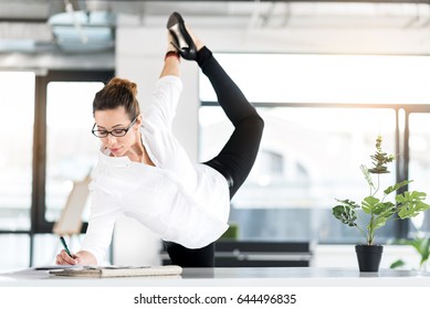 Happy woman making notes while standing near desk in cozy apartment. She making physical jerk near it
