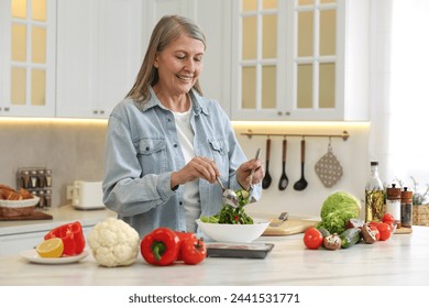 Happy woman making salad at table in kitchen - Powered by Shutterstock