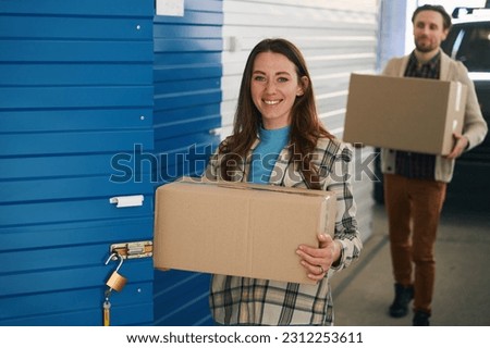 Happy woman and man with big cardboard box into warehouse