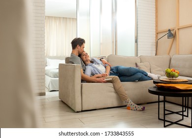 Happy woman and man resting on sofa while switching channels with remote control at home