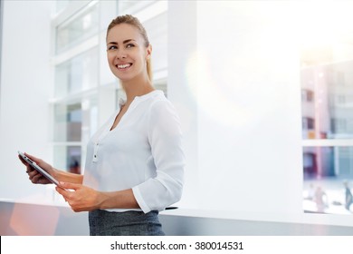 Happy woman manager holding touch pad and thinking about something good while standing in modern office interior,young smart female secretary smiling for someone during work on portable digital tablet - Powered by Shutterstock