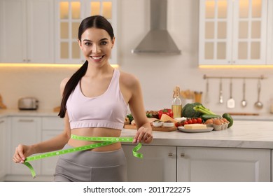Happy woman measuring waist with tape in kitchen. Keto diet