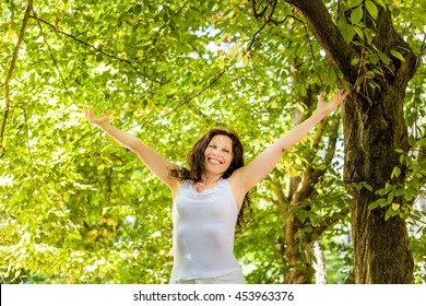 Happy Woman In Menopause Raises Her Arms To The Sky In A Garden, Joyfully Living The Change Of Life